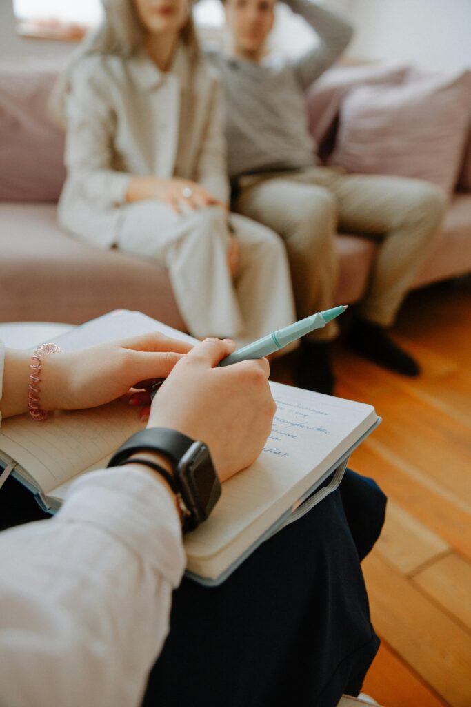 A therapist takes notes while counseling a couple in an indoor session.